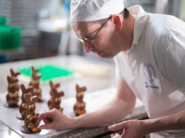 Een chocolatier van Bakkerij Bossuyt werkt paashazen in chocolade met de hand af