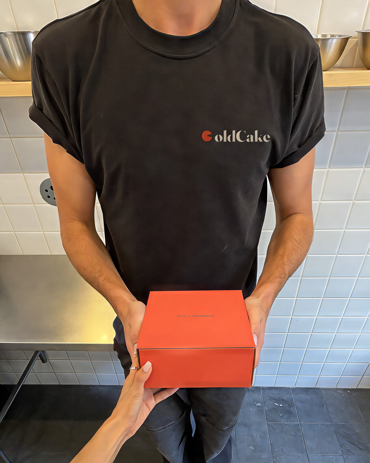 De bezorger in een zwart ColdCake-shirt neemt de koraalkleurige doos aan uit de handen van de bakker.